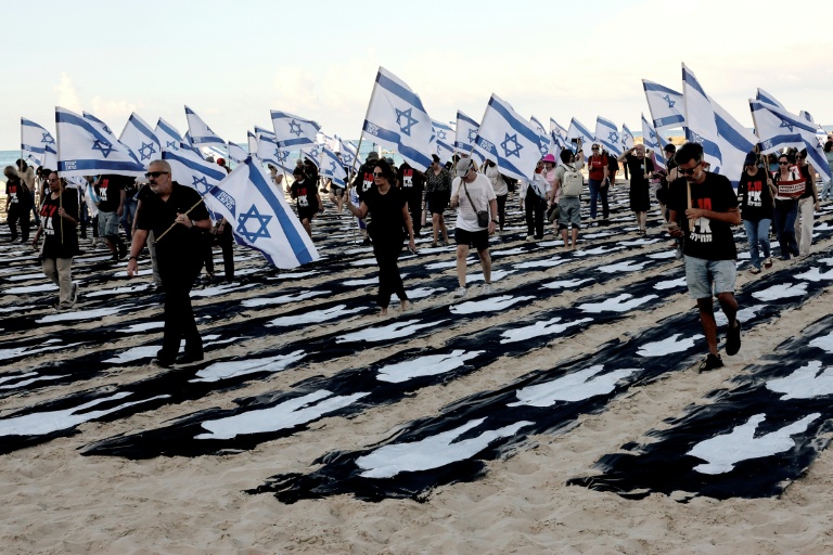 Des personnes portant des drapeaux israéliens traversent une installation commémorative sur la plage de Tel-Aviv pour marquer le troisième anniversaire de l'attaque du Hamas contre Israël, le 7 octobre 2026