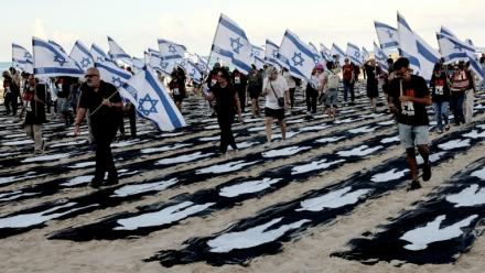 Des personnes portant des drapeaux israéliens traversent une installation commémorative sur la plage de Tel-Aviv pour marquer le troisième anniversaire de l'attaque du Hamas contre Israël, le 7 octobre 2026