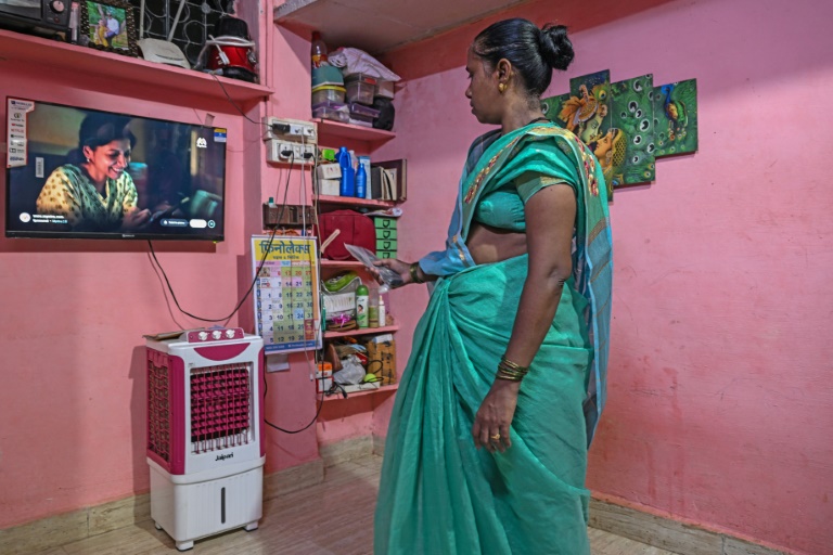 Manda Sunil Bhave, éligible à la relocalisation dans le cadre d'un projet de rénovation urbaine, regarde la télévision chez elle à Dharavi, un bidonville de Bombay, le 9 juillet 2025 en Inde
