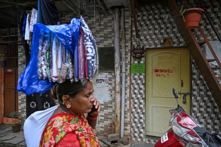 Une vendeuse ambulante passe devant des maisons destinées à être réaménagées dans le cadre d'un projet de rénovation urbaine du bidonville de Dharavi, le 8 juillet 2025 à Bombay, en Inde