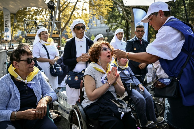 Des volontaires distribuent l'hostie aux fidèles en fauteuils roulants, lors de la messe célébrée par le pape Léon XIV sur la prairie du sanctuaire de Lourdes, le 27 septembre 2026