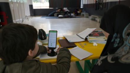 Une femme, assise à côté d'un enfant, supervise ses études en ligne sur un téléphone portable dans une école publique transformée en refuge pour personnes déplacées, à Dekwaneh, au nord de Beyrouth, le 25 mars 2026 au Liban