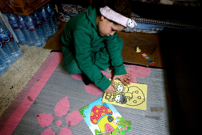 Une fillette colorie un dessin assise par terre dans une salle de classe d'une école publique transformée en refuge pour personnes déplacées, à Dekwaneh, au nord de Beyrouth, le 24 mars 2026 au Liban