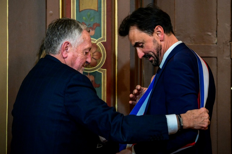 Le maire réélu Grégory Doucet, à droite, reçoit son écharpe des mains de Jean-Michel Aulas, à gauche, le 27 mars 2026, à Lyon