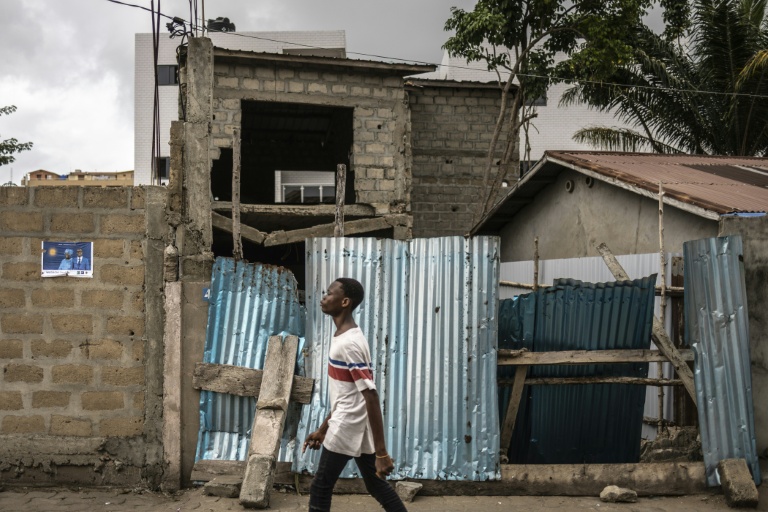 Un jeune homme marche dans un quartier de Cotonou le 9 avril 2026, près d'une affiche électorale placardée au mur 