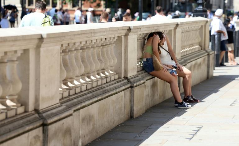 Des personnes se protégent du soleil derrière un mur, le 24 juin 2026 à Londres