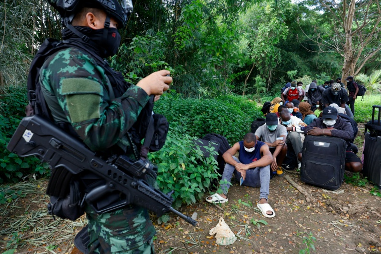 Un soldat monte la garde devant des personnes de différents pays, qui travaillaient au complexe du parc KK en Birmanie et ont traversé la rivière Moei pour se rendre en Thaïlande, dans le district de Mae Sot, dans la province de Tak, le 24 octobre 2025