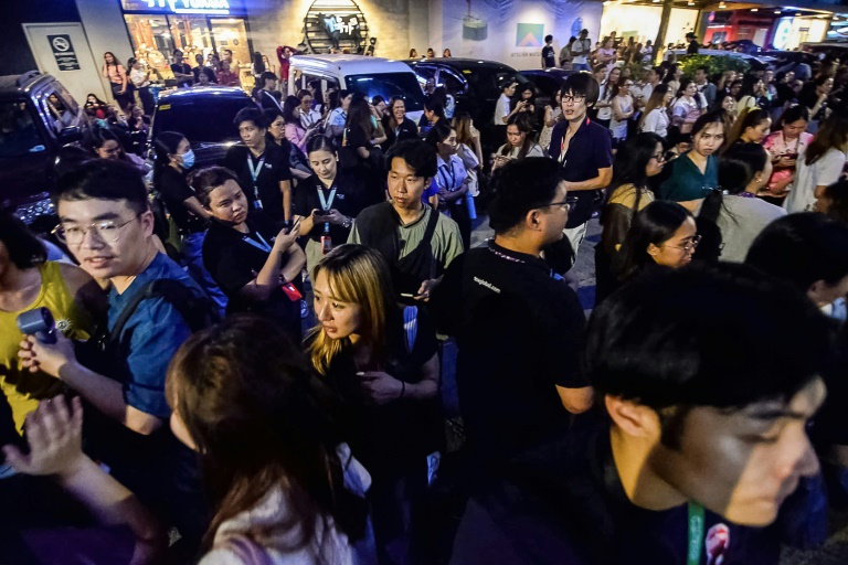 Les employés du centre d'appels surfent sur leurs téléphones portables alors qu'ils se rassemblent devant leur immeuble de bureaux après les secousses du tremblement de terre à Cebu, dans le centre des Philippines, le 30 septembre 2025