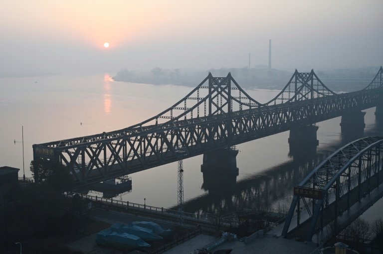 La ville nord-coréenne de Sinuiju, derrière le pont de l'Amitié sino-coréenne (g) et le pont brisé du fleuve Yalu (d), vue depuis la ville frontalière de Dandong, dans le nord-est de la Chine, le 26 mars 2026