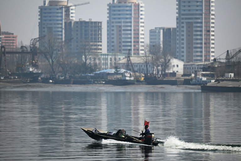 un bateau chinois sur le fleuve Yalu passe devant la ville nord-coréenne de Sinuju, en face de la ville frontalière de Dandong, dans le nord-est de la Chine, le 26 mars 2026