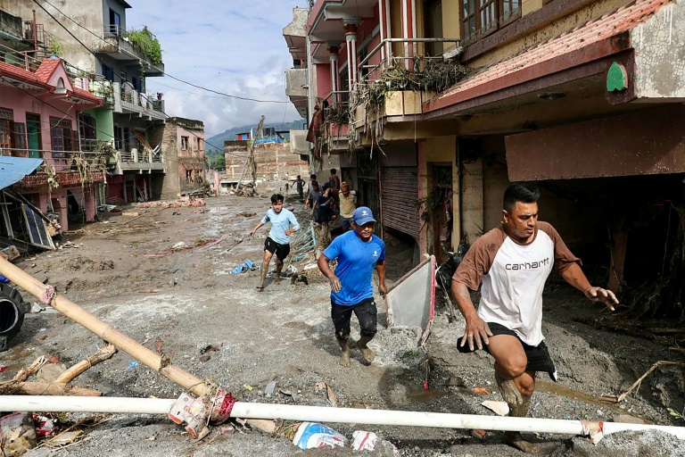 Des habitants passent devant des maisons noyées sous la boue après des crues soudaines à Devighat au Népal, le 27 août 2026