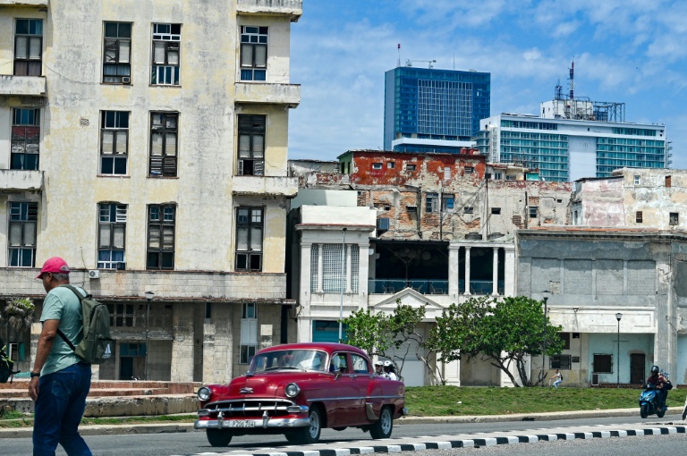 Un homme marche dans la rue tandis qu'une voiture classique passe, avec en arrière-plan l'hôtel Iberostar Selection et l'hôtel Habana Libre Melia, à La Havane, le 2 juin 2026