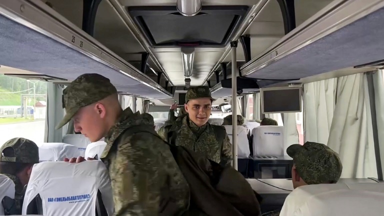 Image tirée d'une vidéo diffusée par le ministère russe de la Défense, le 9 juin 2025, de prisonniers de guerre russes tenant un drapeau russe devant un bus après un échange dans un lieu non divulgué au Bélarus