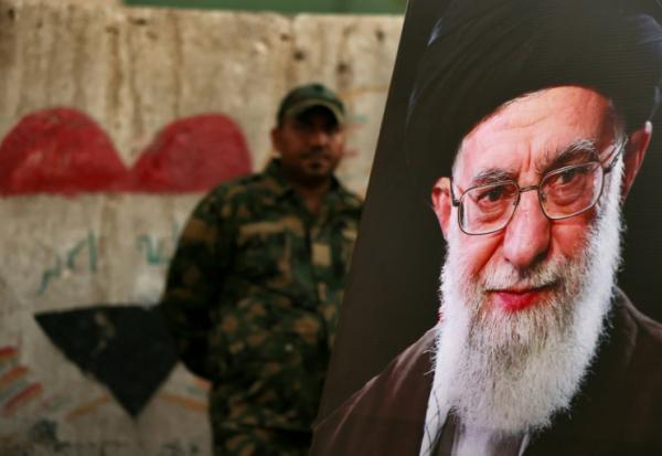 Un membre des Forces de mobilisation populaire irakiennes se tient derrière un portrait du guide suprême iranien défunt Ali Khamenei, à la veille de son cortège funère, au mausolée de l'imam Hussein à Karbala, en Irak, le 7 juillet 2026