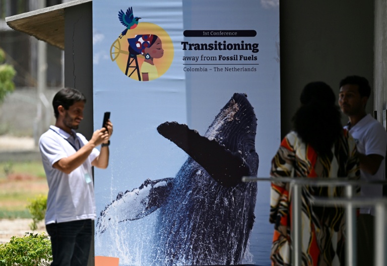 Des personnes prennent une photo devant une affiche de la conférence pour une sortie des énergies fossiles, à Santa Marta, en Colombie, le 26 avril 2026