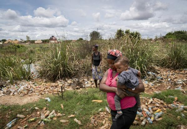 Hélène Mvubu porte sa fille en marchant dans un champ pollué à Lubumbashi en République démocratique du Congo le 24 novembre 2025