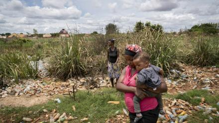 Hélène Mvubu porte sa fille en marchant dans un champ pollué à Lubumbashi en République démocratique du Congo le 24 novembre 2025