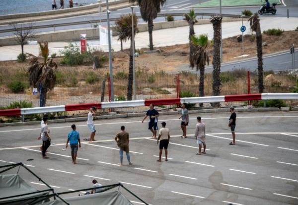 Des migrants jouent au foot sur un parking près d'abris temporaires installés pour eux, le 27 août 2026 à Ceuta