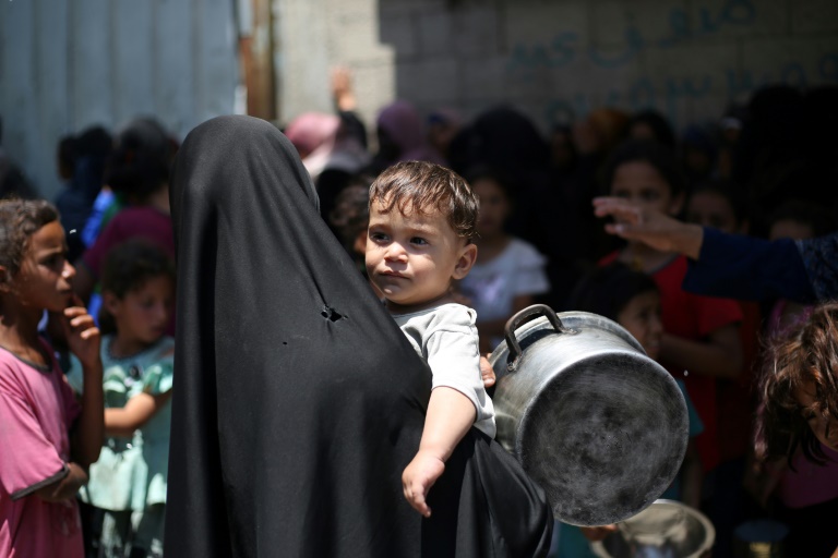Une Palestinienne portant un enfant dans une file d'attente à un distribution de repas chauds à Nousseirat, dans le centre de la bande de Gaza, le 4 juin 2025