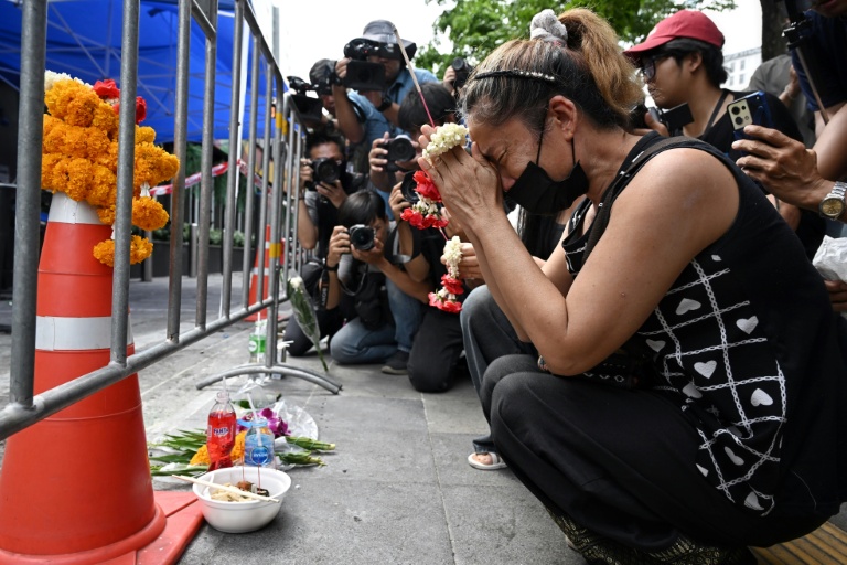 Une femme endeuillée prie sur les lieux de l'incendie dans le bar Rong Beer Na Lat Phrao, le 14 juillet 2026 à Bangkok, en Thaïlande