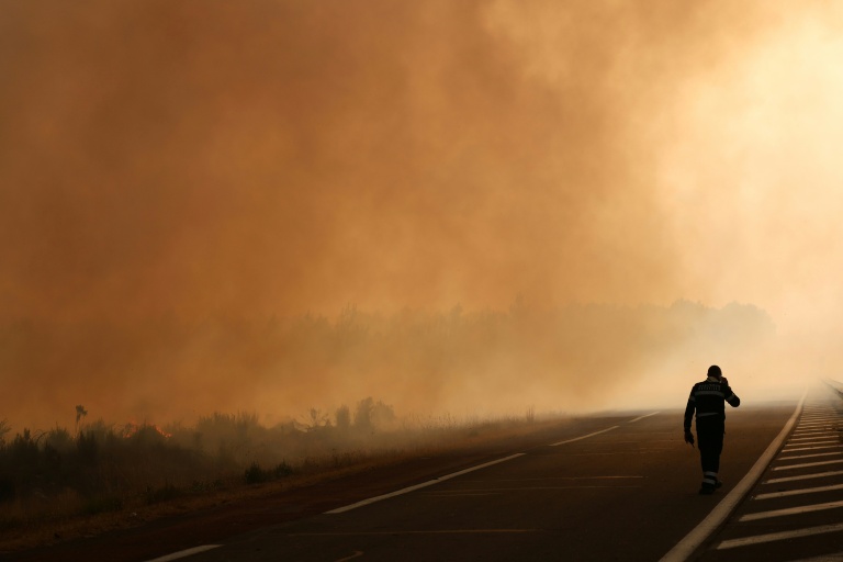 Un pompier marche sur une route à la lisière d'une zone en feu à Ares, le 26 juillet 2026, alors qu'un incendie de forêt ravage la forêt au nord du bassin d'Arcachon (Gironde) depuis le 22 juillet