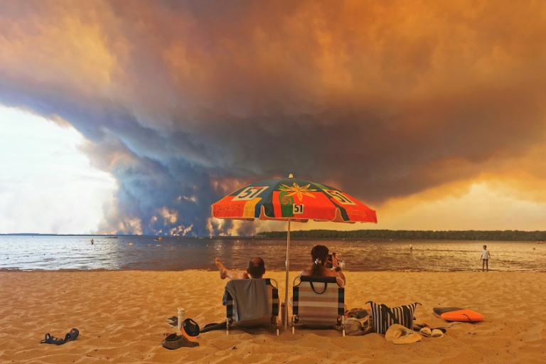 Des personnes sur la plage du Moutchic à Lacanau, dans le sud-ouest de la France, le 24 juillet 2026, tandis que des nuages de fumée d'un incendie s’élèvent dans le ciel 