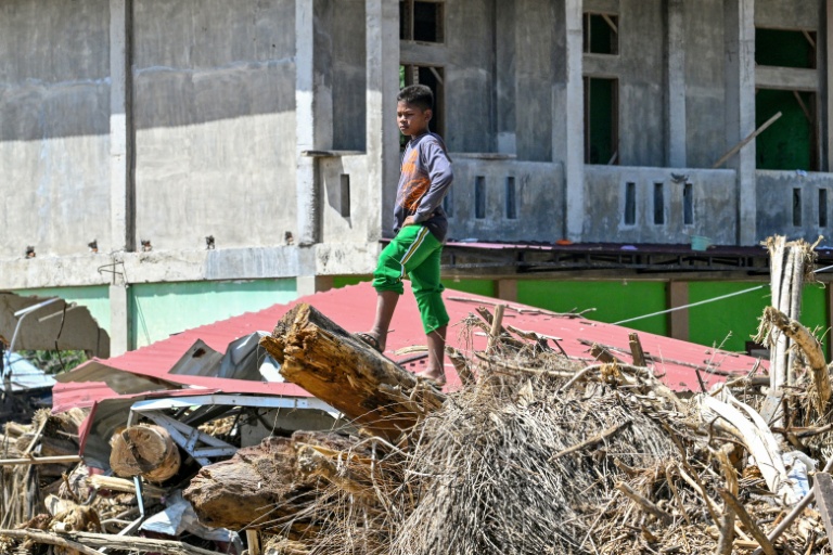 Un enfant debout sur des débris d'arbres après des crues soudaines à Meureudu, dans province d'Aceh, en Indonésie, le 8 décembre 2025