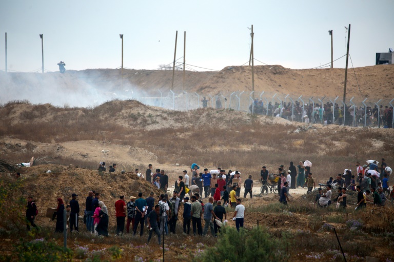 Des Palestiniens déplacés se dirigent vers un centre de distribution d'aide humanitaire, alors que des bombes fumigènes sont tirées par les troupes israéliennes, dans le centre de la bande de Gaza, le 8 juin 2025