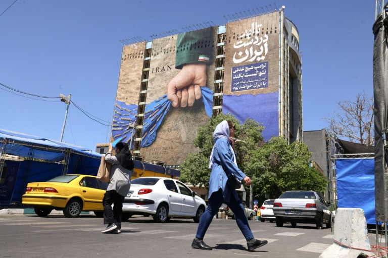 Des passants près d'un panneau d'affichage sur la façade d'un immeuble représentant le détroit d'Ormuz avec une inscription en persan disant 
