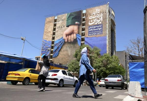 Des passants près d'un panneau d'affichage sur la façade d'un immeuble représentant le détroit d'Ormuz avec une inscription en persan disant "À jamais dans la main de l'Iran", place Vanak à Téhéran, le 25 mai 2026