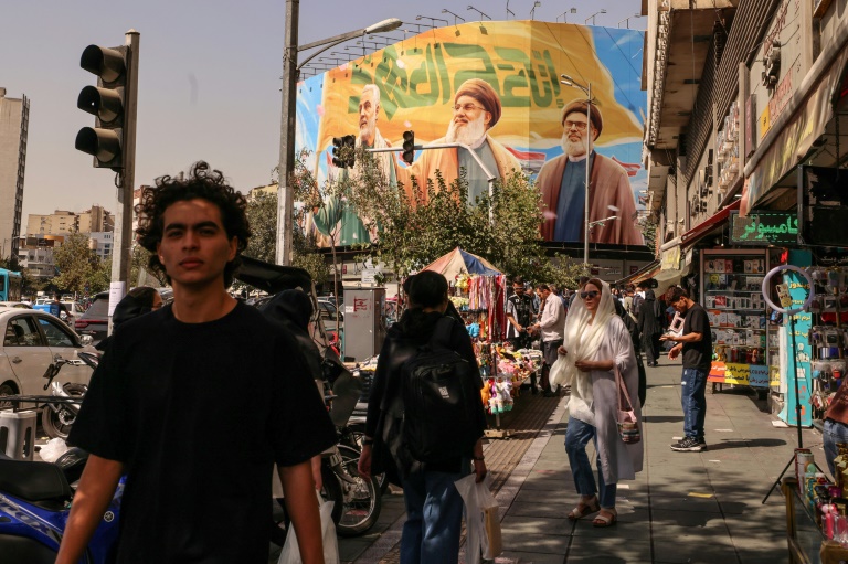 Des passants devant un panneau d'affichage représentant les dirigeants libanais du Hezbollah assassinés Hassan Nasrallah (C) et son successeur Hachem Safieddine (D), ainsi que le général iranien Qassem Soleimani, à Téhéran, le 28 septembre 2025