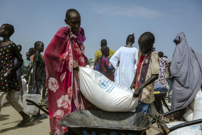 Un garçon et sa mère soulèvent un sac de maïs pour le charger dans leur brouette, dans un centre de distribution du camp de déplacés à Bentiu, dans l'État d'Unity, au Soudan du Sud, le 6 novembre 2025