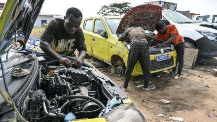 Des mécaniciens informels travaillent sur des moteurs de voiture dans le quartier d'Angré, à Abidjan, la capitale économique ivoirienne, le 21 juillet 2026.