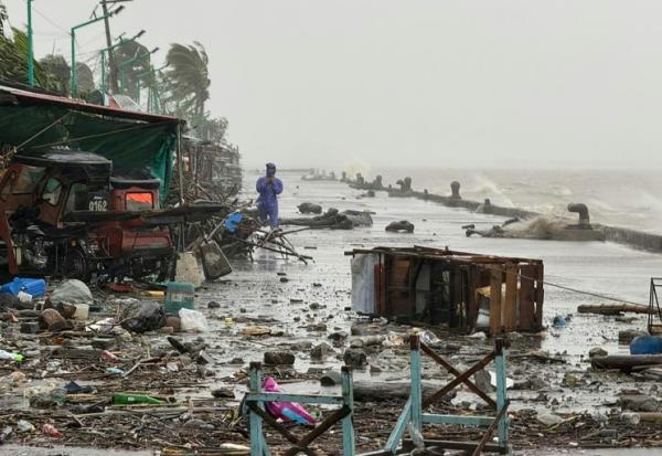 Un homme se tient à côté de débris près du bord de mer, le 22 septembre 2025 à Aparri aux Philippines