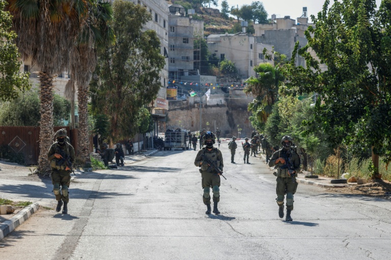 Des soldats israéliens patrouillent dans une rue de Qusra, en Cisjordanie occupée, où des colons israéliens assiègent des maisons palestiniennes, le 13 août 2026