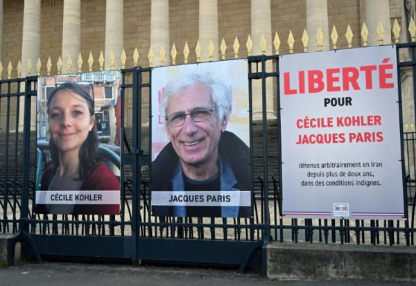 Des portraits exposés de Française Cécile Kohler (G) actuellement emprisonnée en Iran avec son partenaire, le Français Jacques Paris (C) devant le Palais Bourbon, l'Assemblée nationale française à Paris, le 25 mars 2025