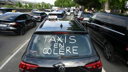 Un slogan "Taxis en colère" est inscrit sur une voiture alors que des chauffeurs de taxi participent à une opération de blocage à Pau, 
le 19 mai 2025