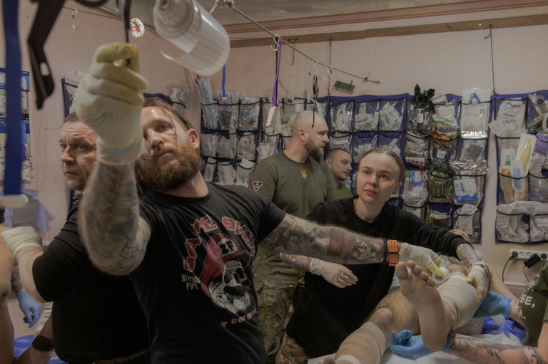 Anastassia Podobailo (d), son collègue et époux Mykola Iassinenko (2e g) et d'autres médecins militaires, soignent un soldat blessé dans un poste médical de la 56e brigade, dans la région de Donetsk, le 15 mars 2026 en Ukraine