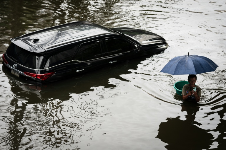 Un homme passe devant uen voiture sous les eaux à Bangkok, où l'état de catastrophe naturelle a été déclaré après des pluies diluviennes qui ont inondé habitations, commerces et axes de circulation, le 27 septembre 2026