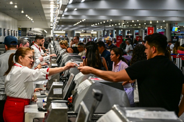 Des voyageurs présentent leurs documents aux personnels d'une compagnie aérienne à l'aéroport international de Miami, le 24 mai 2025 en Floride
