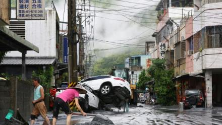 Des habitants nettoient la boue devant chez eux, avec des véhicules renversés en arrière-plan, après la rupture d'une digue au passage du super typhon Ragasa, à Hualien à Taïwan, le 24 septembre 2025