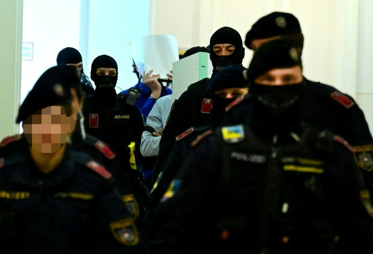 Deux accusés, escortés par des policiers, cachent leurs visages à leur arrivée à la salle d'audience du tribunal de Wiener Neustadt, en Autriche, le 28 avril 2026, pour un projet d'attentat lors d'un concert de Taylor Swift à Vienne